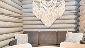 A log cabin interior with a gray sofa, two patterned pillows, and a white table with a candle. - Korvenpää by Interhome (Joutsa)