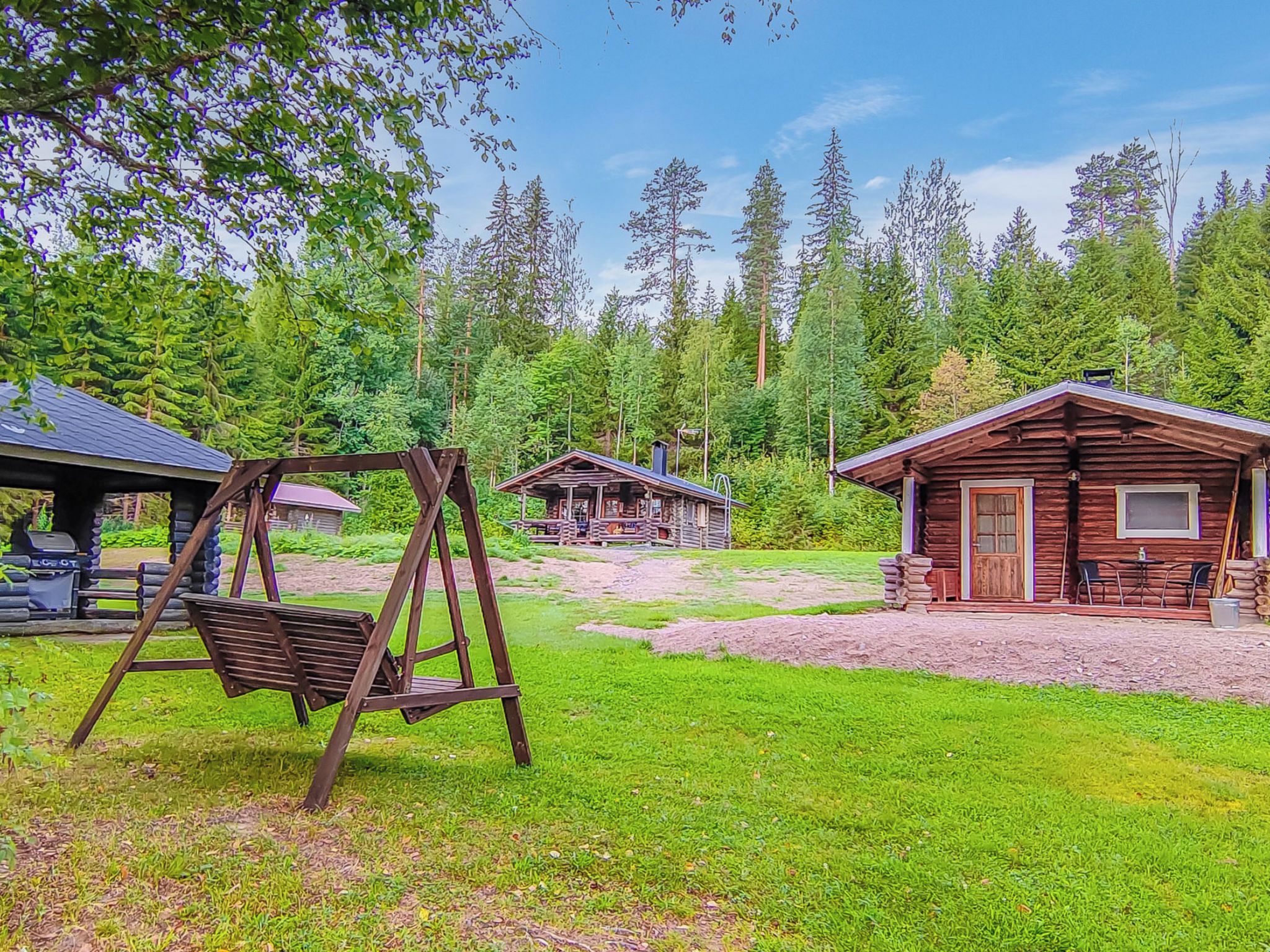 A rustic cabin with a porch and a swing set in a forested area.