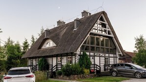 Une maison traditionnelle à toit de chaume, dotée d’une grande fenêtre et d’un escalier en pierre menant à l’entrée.