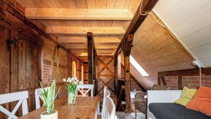 Une pièce mansardée chaleureuse avec des poutres apparentes, une table en bois avec des chaises, un canapé blanc et un petit lit.