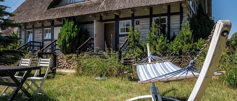 A rustic house with a thatched roof, a wooden porch, and a hammock in the front yard.