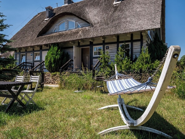 A rustic house with a thatched roof, a wooden porch, and a hammock in the front yard.
