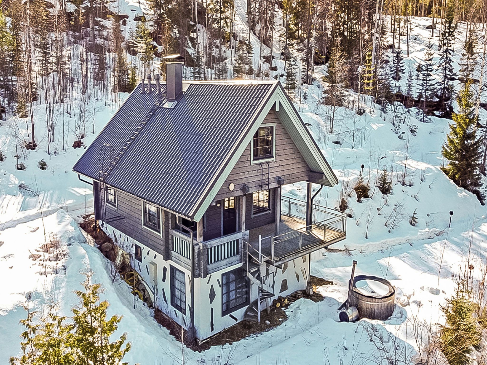 Una cabaña de dos pisos con balcón, rodeada por un bosque nevado.