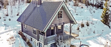A two-story cabin with a balcony, surrounded by a snowy forest.