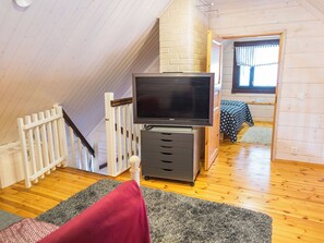A loft-style room with a television on a stand, a small desk, and a window with curtains.