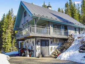 Un chalet à deux étages doté d’un balcon, d’un local pour le matériel de ski et d’un terrain enneigé.