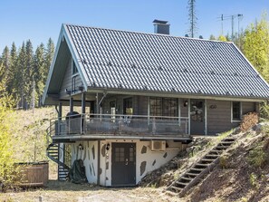 A two-story house with a steeply pitched roof, a balcony, and a staircase leading to the upper level.