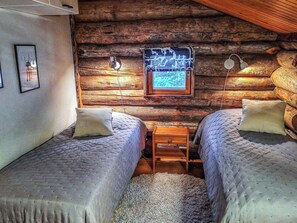 A log cabin bedroom with two beds, a small table, and a framed picture on the wall.
