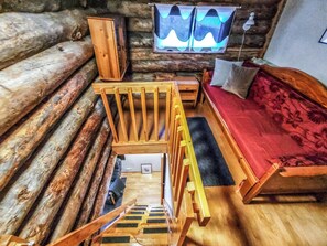 A log cabin interior with a wooden bed, a bench, and a small table.