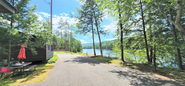 A cabin with a picnic table and red umbrella, surrounded by trees and a lake. - Riverview Cottages # 1 (Lake Luzerne)