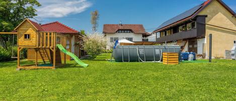A residential property with a wooden playhouse, a green slide, a large water tank, and a house with a red roof.