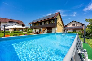 Una piscina con superficie de agua azul cristalina, rodeada por un césped cuidado y un edificio de dos pisos con balcón.