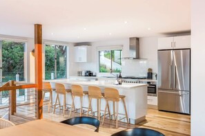 Una cocina moderna con una isla grande, taburetes de bar, electrodomésticos de acero inoxidable y ventanas amplias.