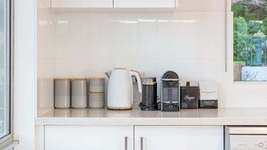 Een keuken met witte kasten, een waterkoker, een koffieapparaat en suikerpotjes.