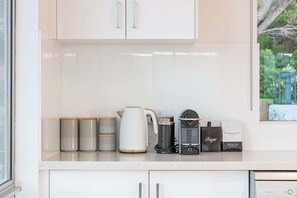 Ett kök med vita skåp, en vattenkokare, en kaffemaskin och behållare för socker.