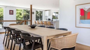 Een moderne keuken met een lange tafel en stoelen, een zithoek met uitzicht en een groot raam.