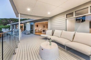 Un espacio exterior moderno con barandilla de vidrio, una mesa redonda blanca y un sofá color beige.