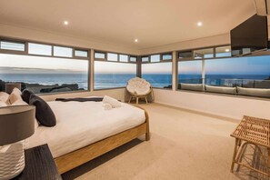Un dormitorio con una cama grande, una silla y vista al océano.