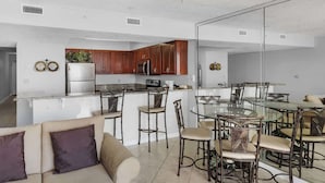 Una cocina moderna con armarios de madera, un refrigerador y un comedor con mesas y sillas de vidrio.