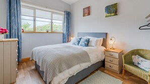 Ein Schlafzimmer mit Bett, Nachttisch, Lampe, Stuhl und einem Kunstwerk an der Wand.