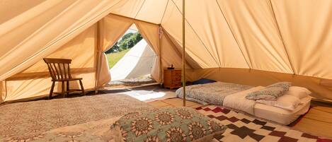 A tent with two beds, a chair, and a small wooden cabinet.