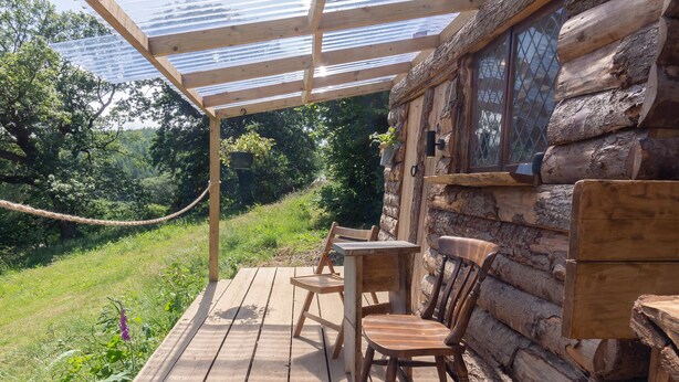 Una terraza de madera con techo de vidrio, sillas de madera y una mesa.