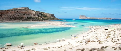 Una playa con aguas turquesas cristalinas, afloramientos rocosos y una montaña distante.