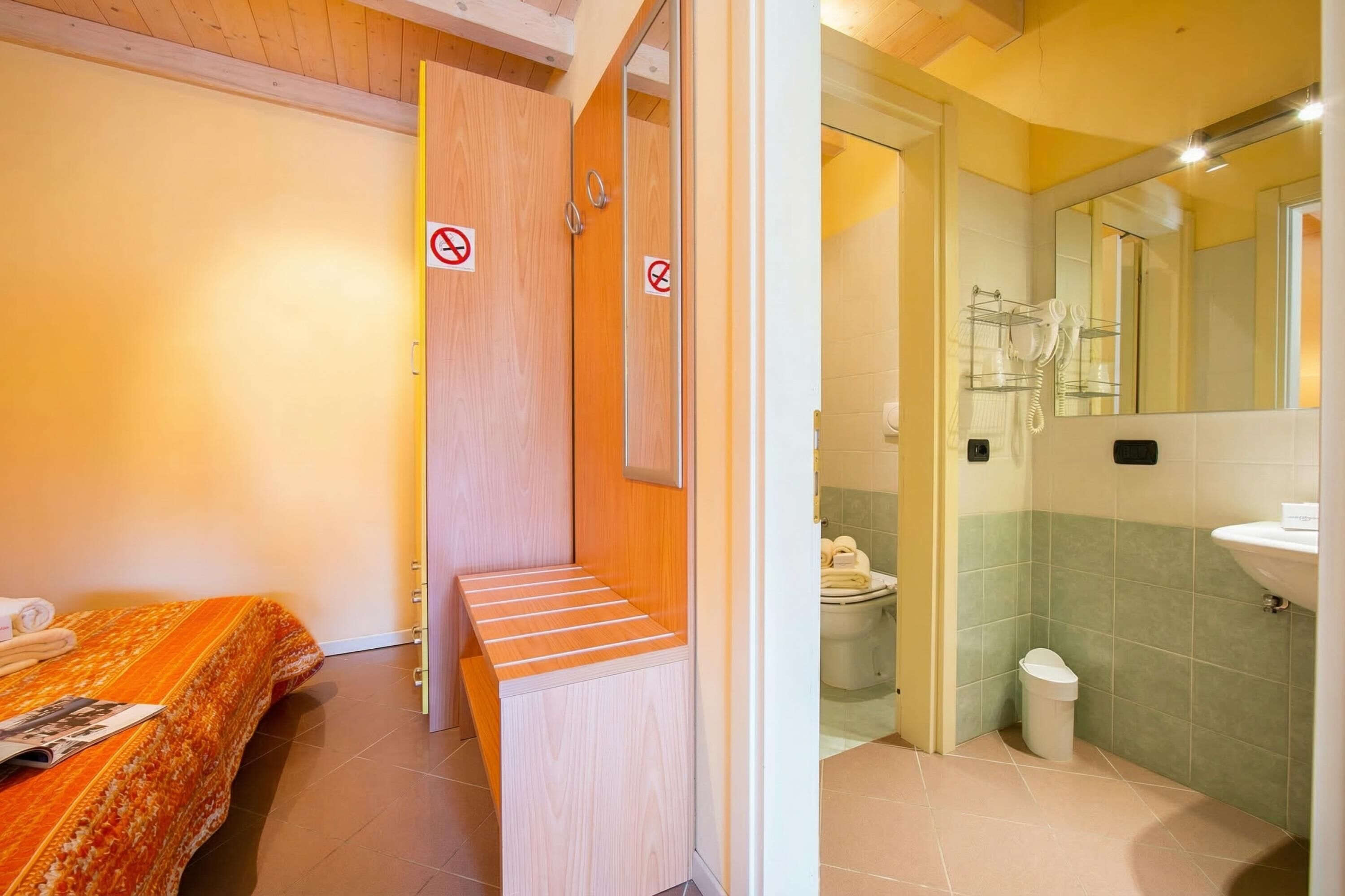A hotel room with a bed, a bench, a bathroom with a sink, and a toilet.