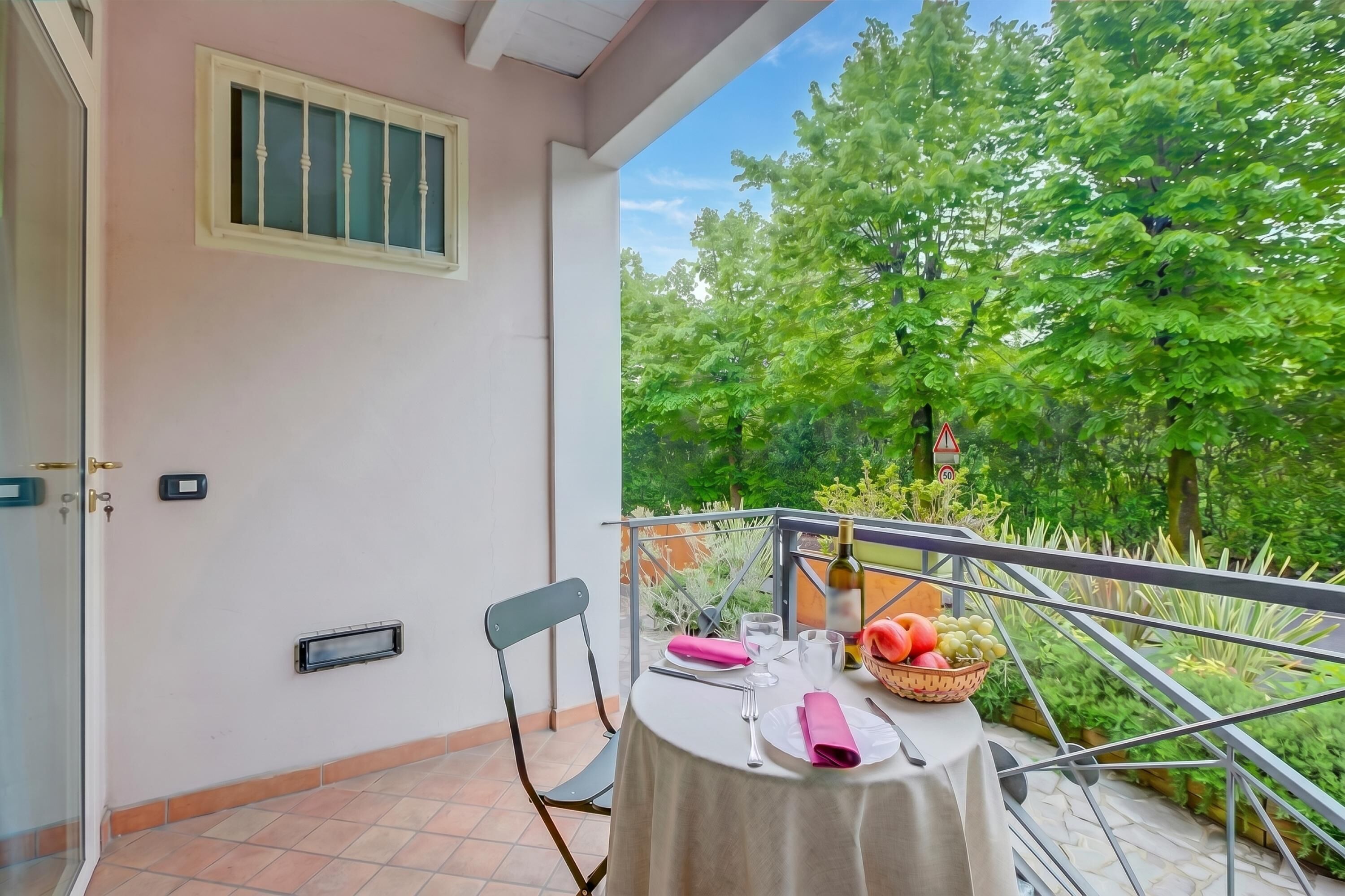 A balcony with a table set for dining, a chair, a window with bars, and a view of lush greenery.