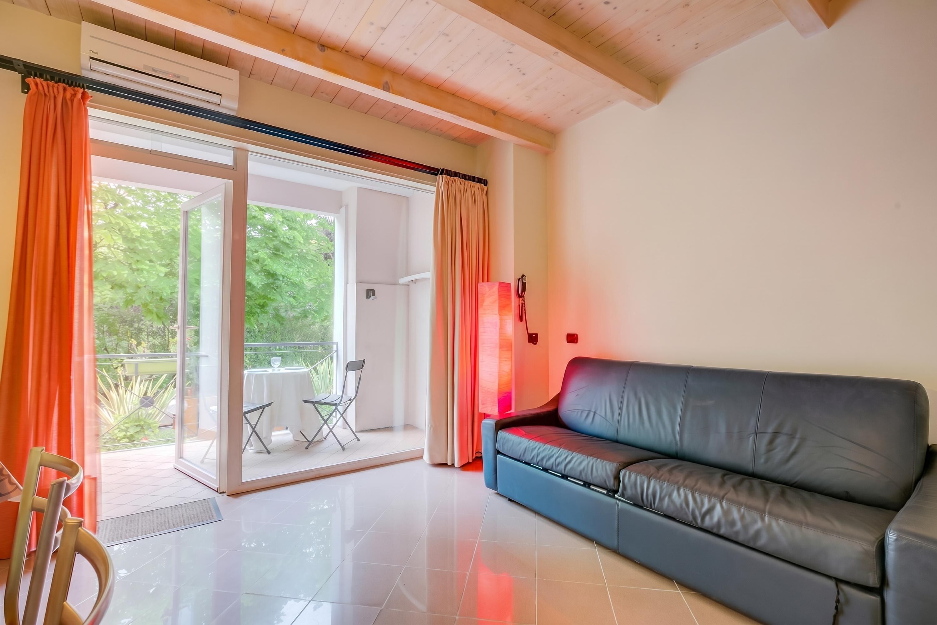 A living room with a sofa, a table, and a chair. There is a sliding glass door leading to an outdoor area with a table and chairs.