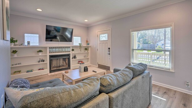 A modern living room with a fireplace, a flat-screen TV, and a large window with blinds. - Pet-Friendly Sacramento Home ~ 5 to Downtown! (Sacramento)