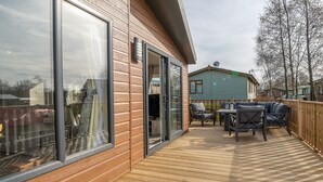 Una terraza de madera con mobiliario exterior, una puerta corrediza de vidrio y vista a una casa vecina.
