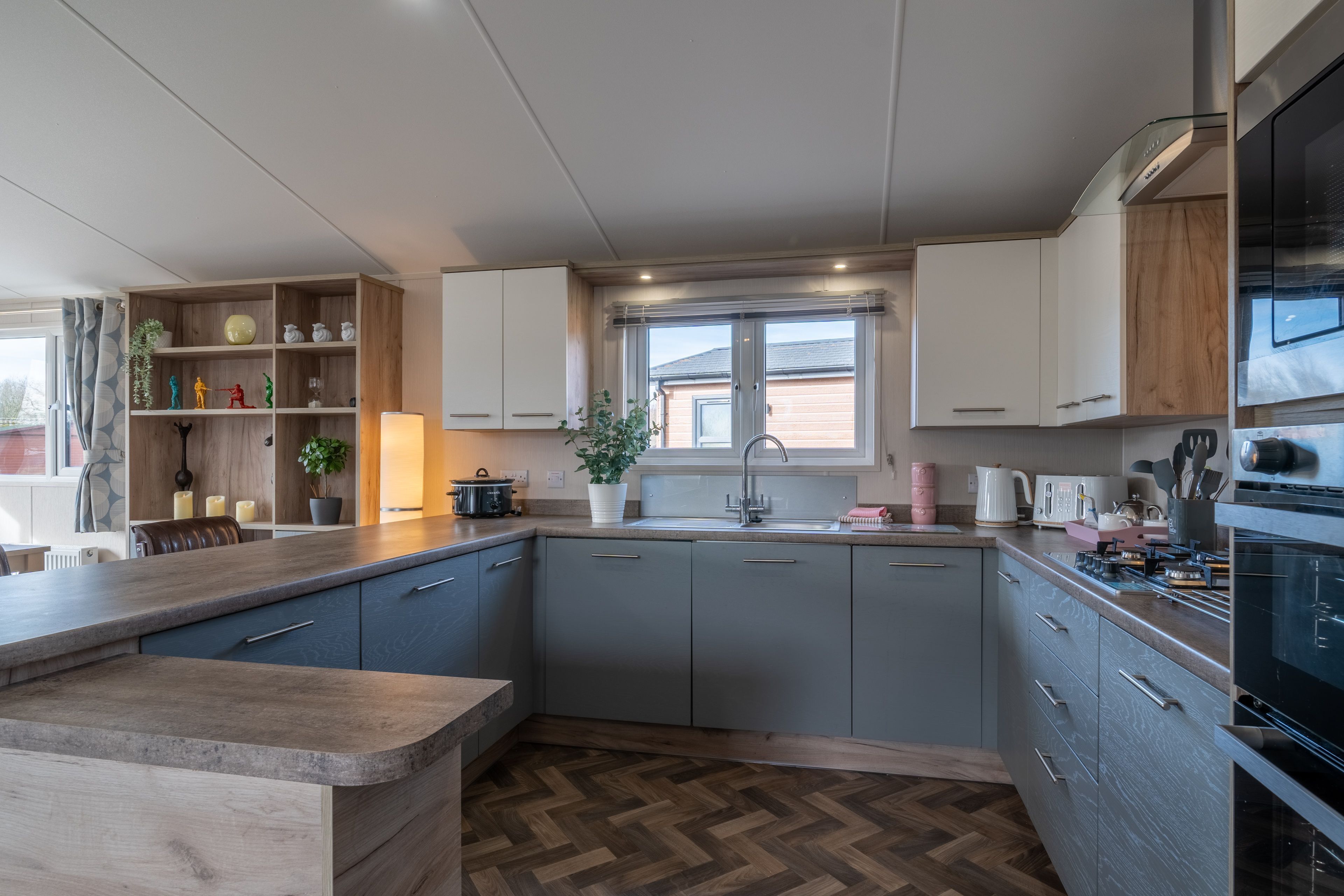 A modern kitchen with grey cabinets, a wooden countertop, and a herringbone floor pattern.