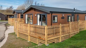 Una hilera de cabañas de madera con terraza amurallada, cada una con puerta y ventanas, en un camping.