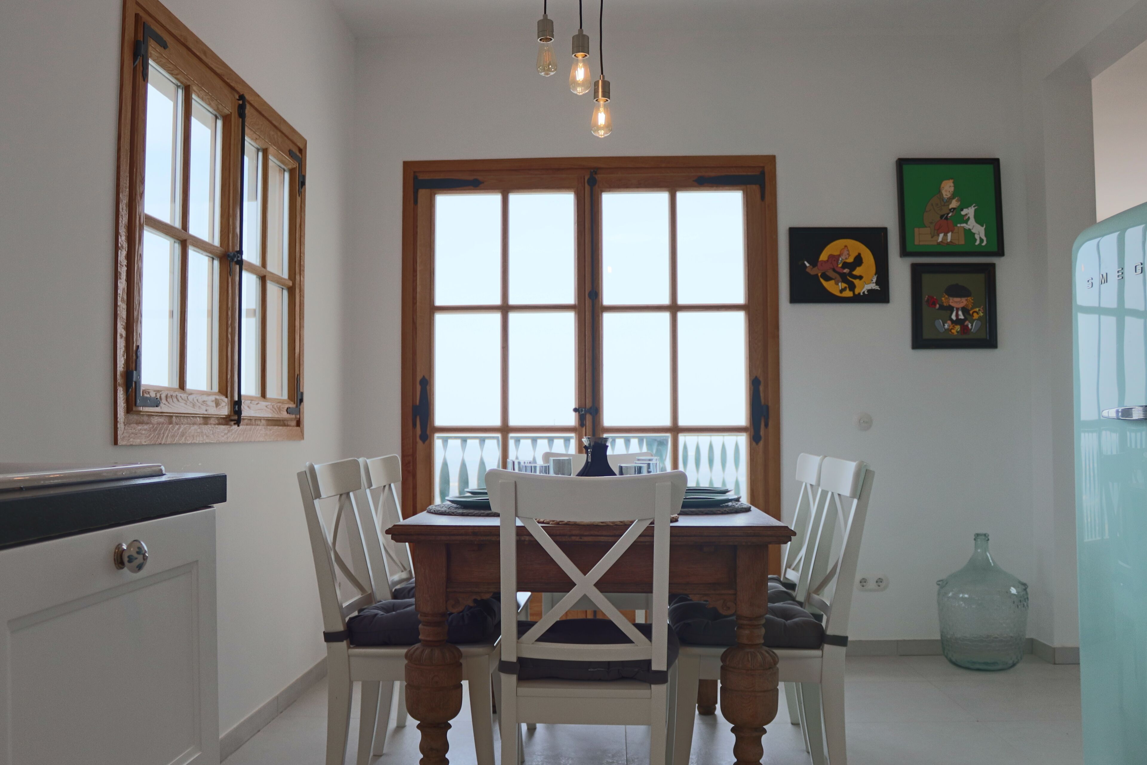A dining area with a wooden table, white chairs, and a large window with multiple panes.