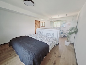 Un dormitorio con una cama, suelo de madera, una planta en maceta y un espejo en la pared.