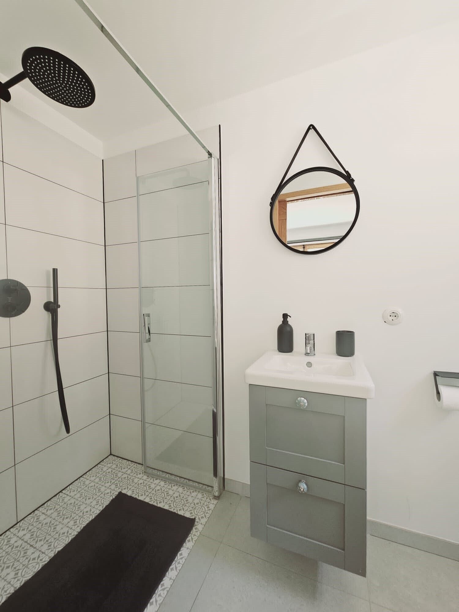Un baño moderno con cabina de ducha de vidrio, tocador con espejo y ducha con cabezal negro.