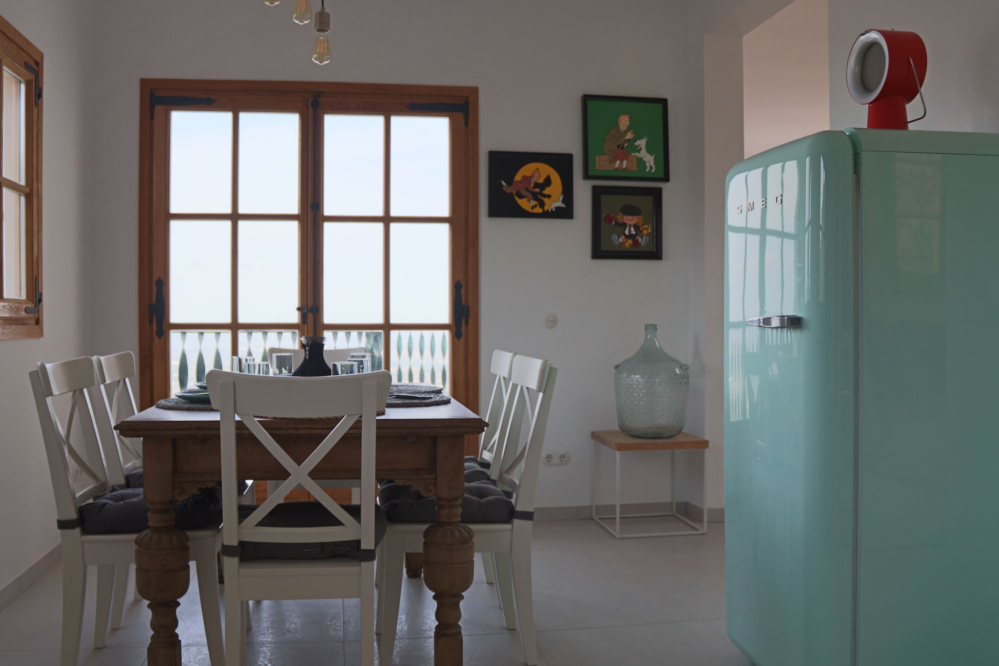 A dining area with a wooden table and white chairs, a vintage teal refrigerator, and artwork on the walls.