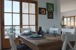 Un comedor con una mesa de madera, sillas blancas y vistas amplias por las ventanas.