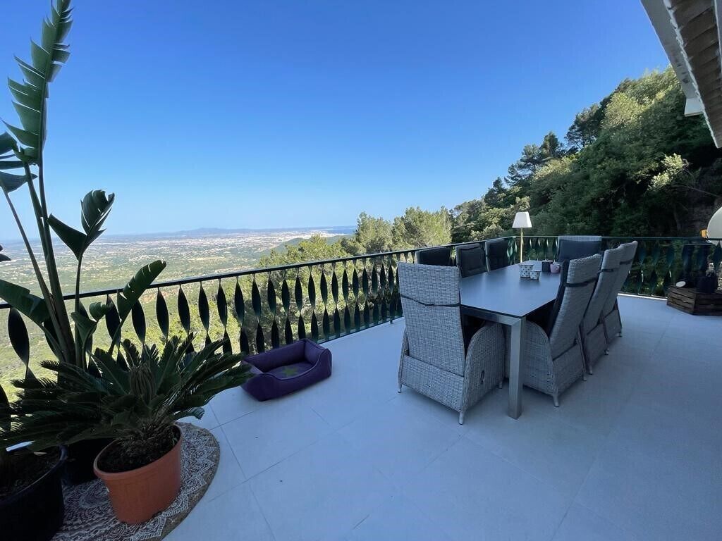 Uma varanda com mesa e cadeiras, vasos de plantas e vista para a paisagem.