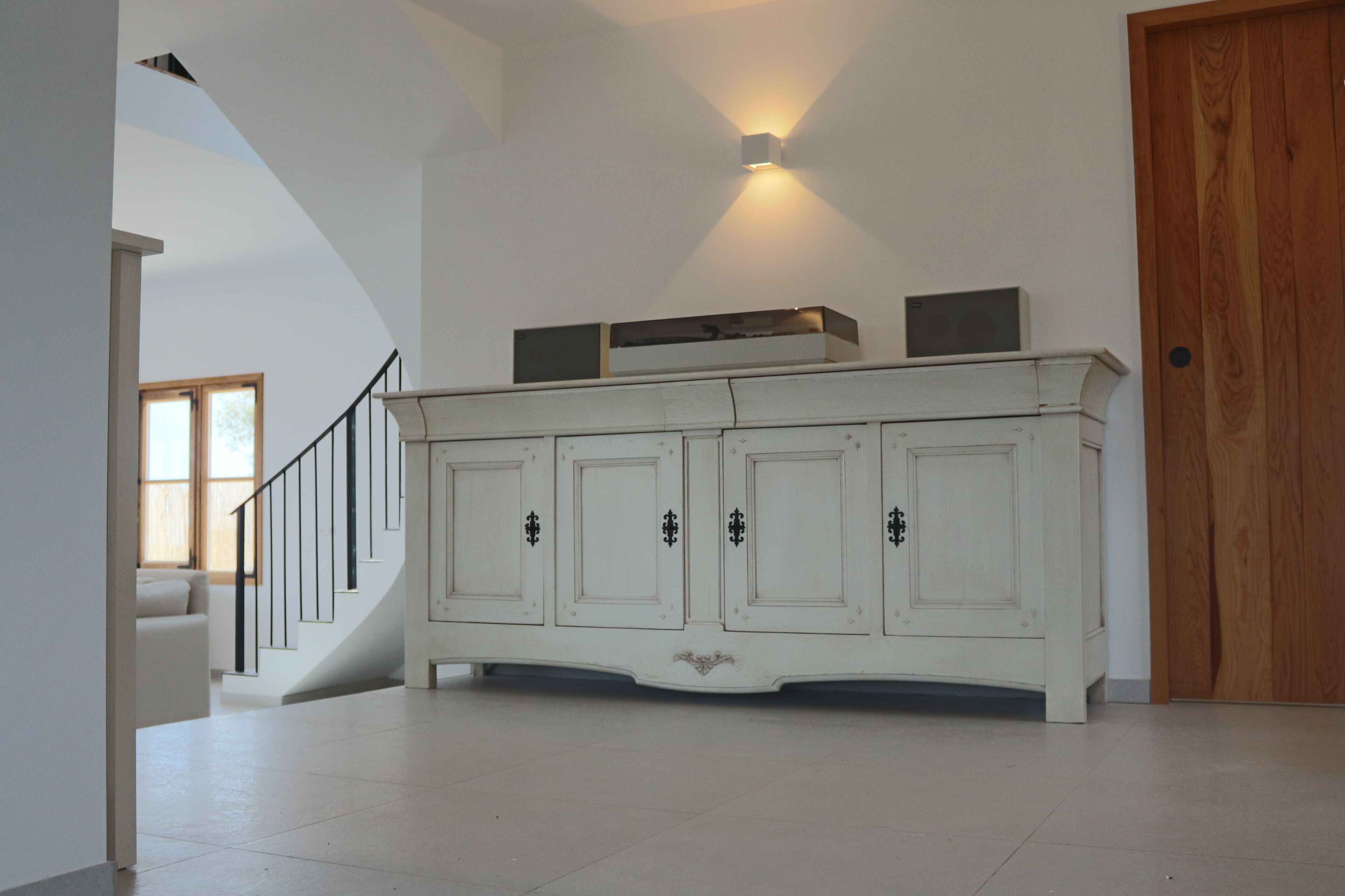 A spacious room with a white cabinet, a staircase, and a wooden door.
