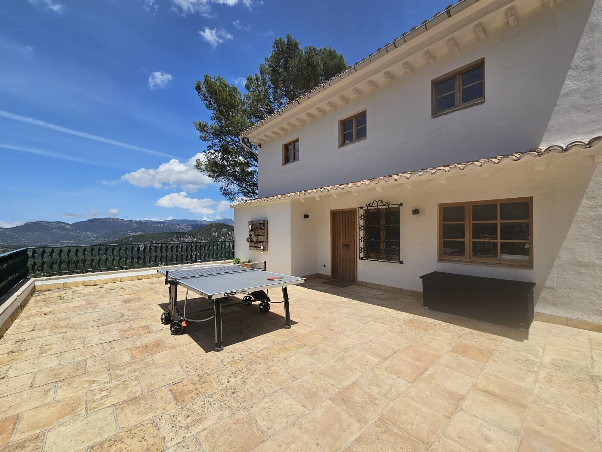 A house with a tennis table on a patio, a view of mountains, and a white exterior.