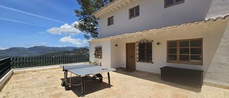 A house with a tennis table on a patio, a view of mountains, and a white exterior.