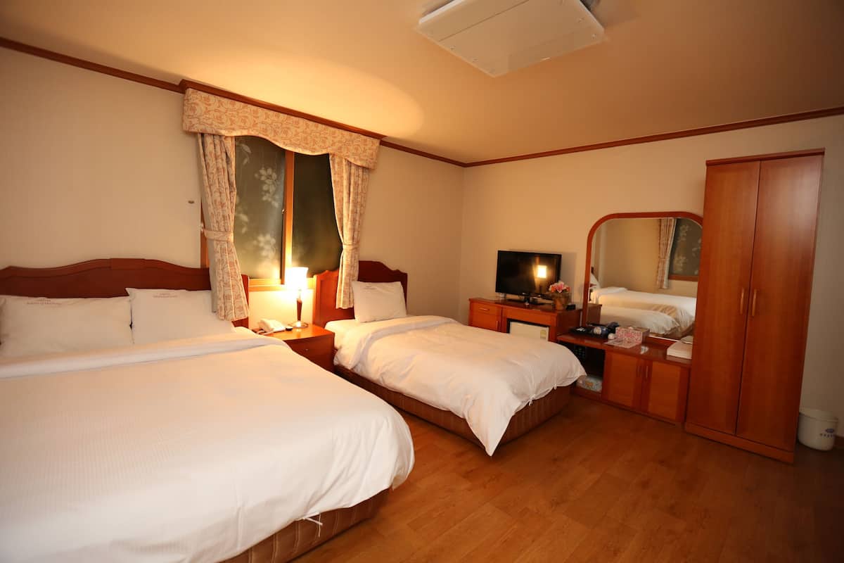 A hotel room with two beds, a wardrobe, a television, and a mirror.