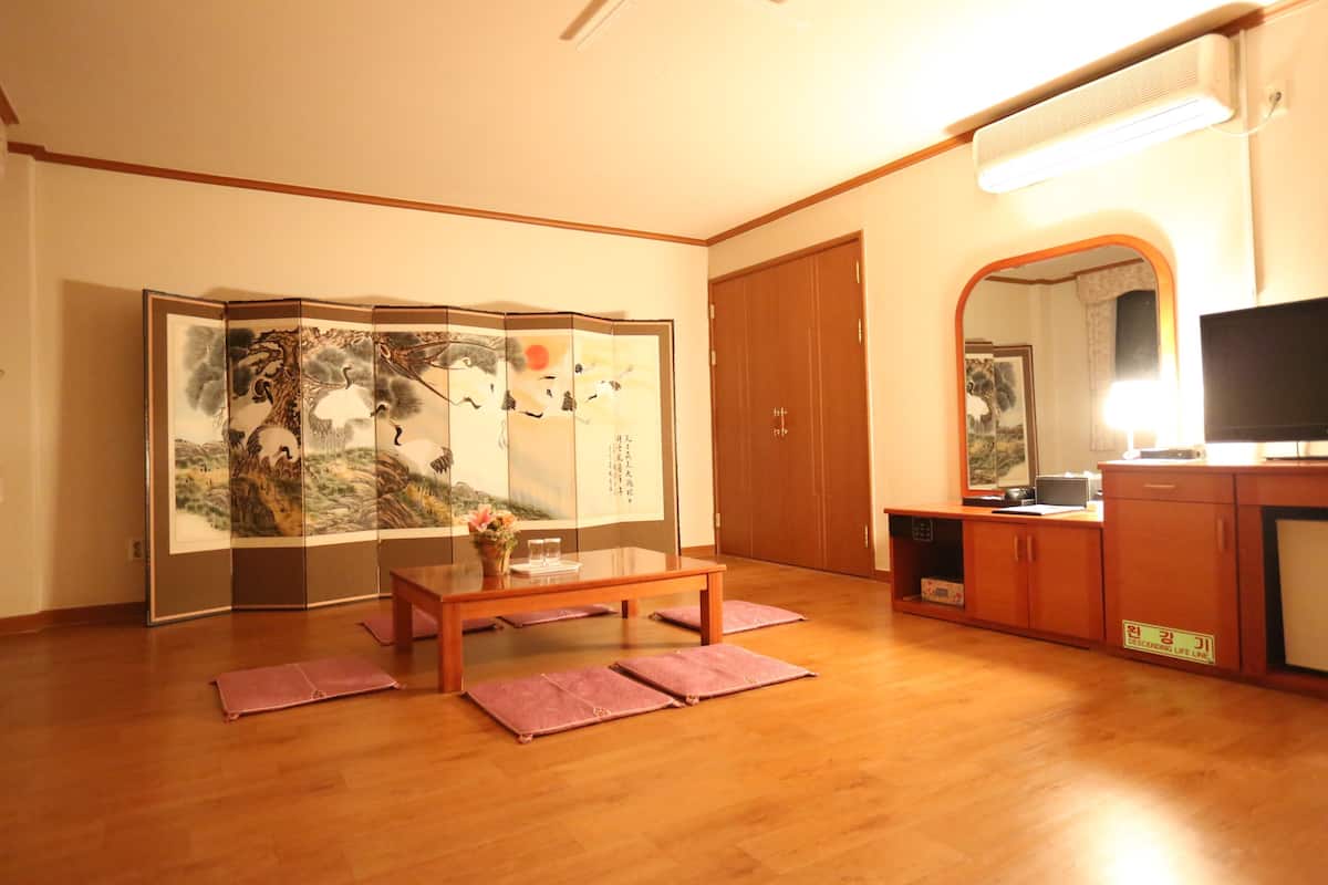A traditional Japanese room with tatami flooring, a low wooden table, a folding screen with artwork, a television, and a cabinet.