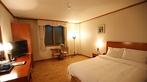 Ein Hotelzimmer mit Holzschreibtisch, Fernseher, einem Bett mit weißer Bettwäsche, einer Schreibtischlampe und einem fenster mit Vorhängen.