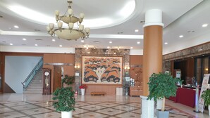 Eine geräumige Lobby mit einer großen Wandmalerei, einem prächtigen Kronleuchter und einer Treppe.