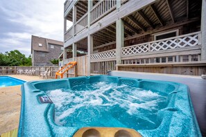 Relax in the hot tub on the outdoor deck, surrounded by a pool and a building with a balcony.