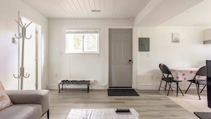 En stue med sofa, sofabord, spisebord med stole, knagerække, dør og vindue.