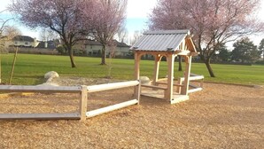 Et trælegeland med tag i en park, med træer og huse i baggrunden.